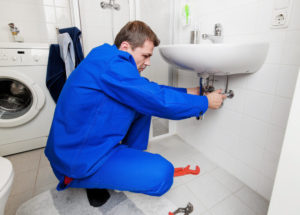 man in blue outfit under sink fixing pipe